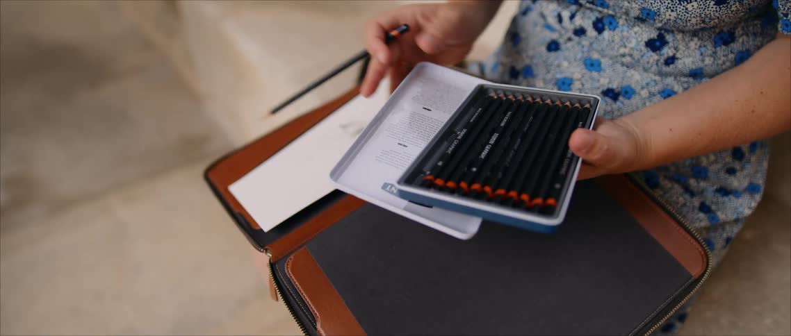 Close up of a young woman selecting a pencil from a case for sketching while sitting outdoors during daytime