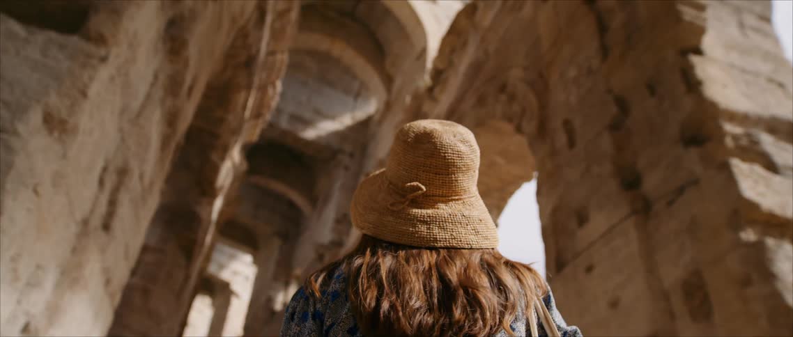 A woman in a sunhat looks up at ancient stone ruins during daylight