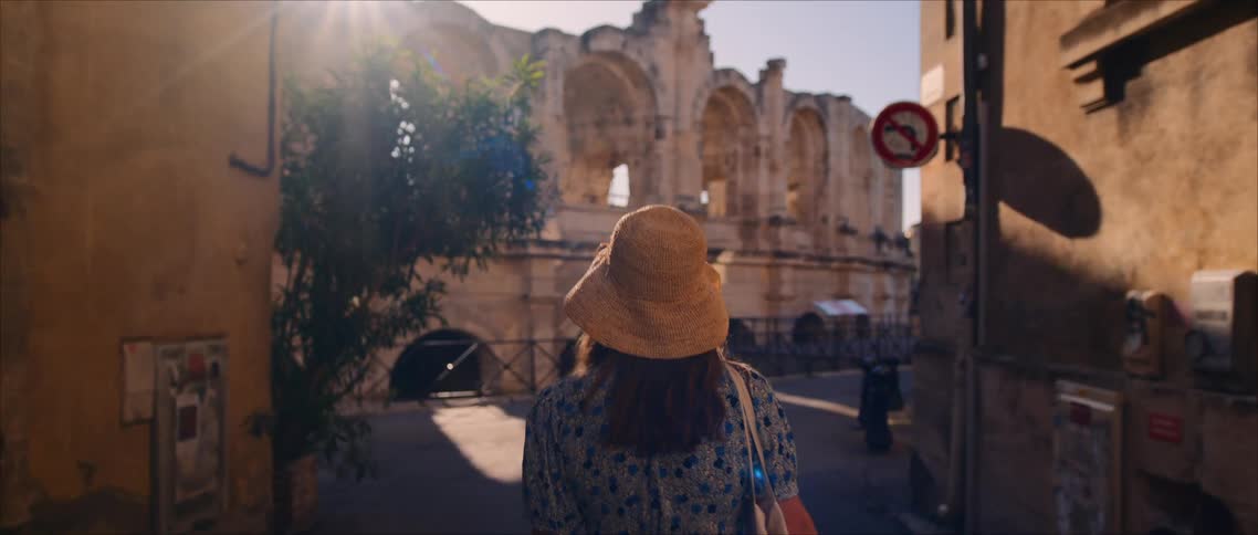 Woman walking down a narrow street toward ancient ruins under the afternoon sun
