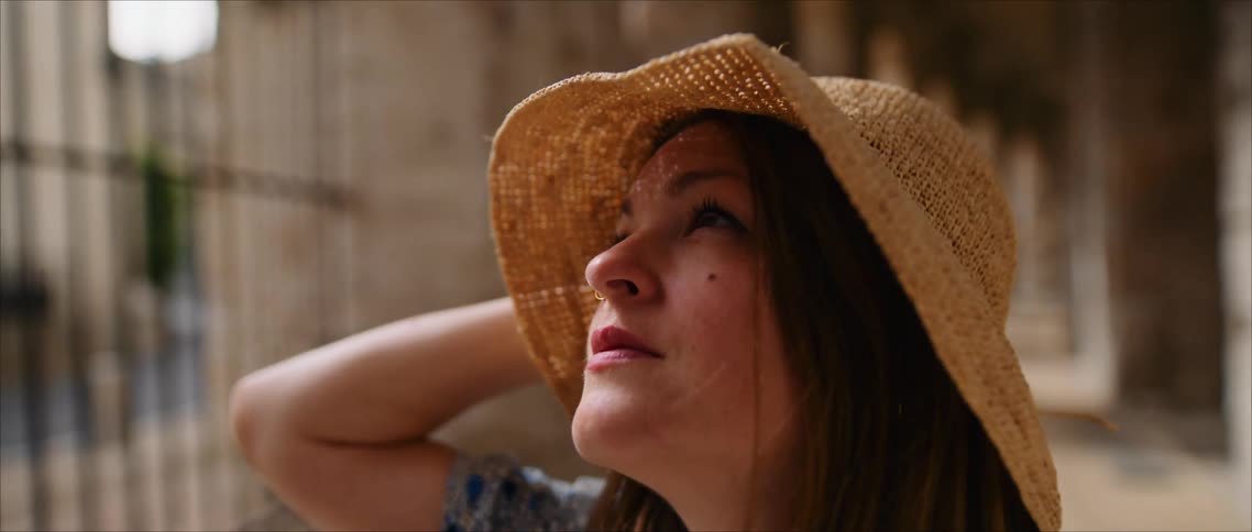 Woman keeps her sunhat on her head as she looks around while near a colonnade
