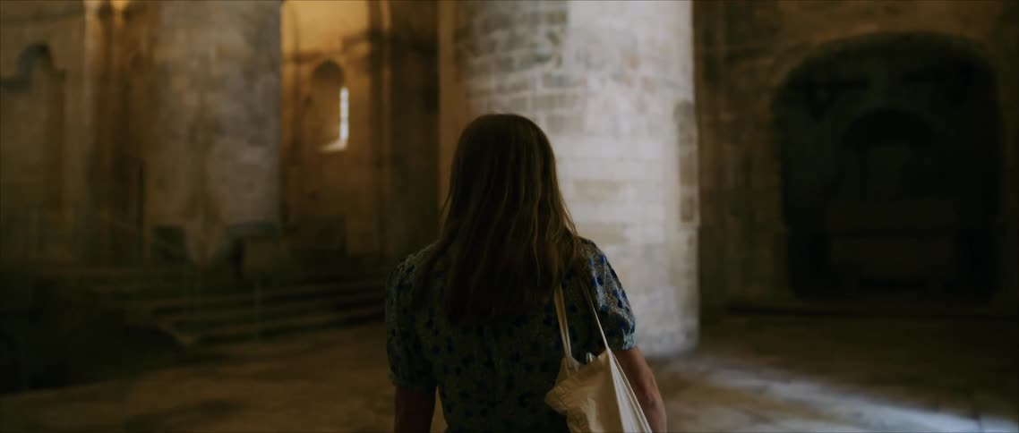 Woman in blue dress observes historic architecture in naturally lit stone interior