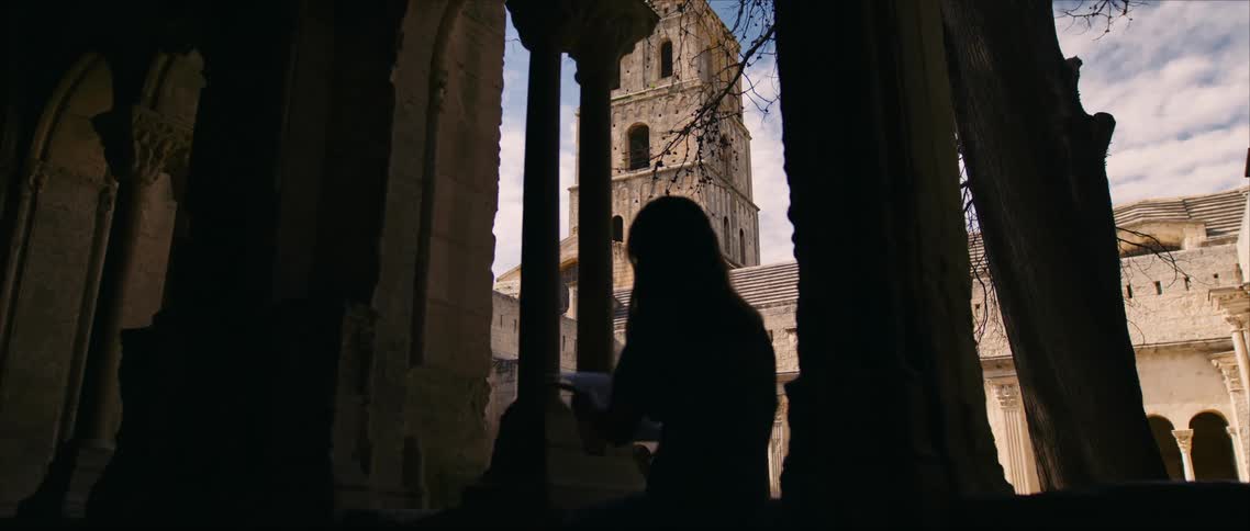 Silhouette of woman seated among ancient columns gazes at tower beyond bathed in soft light and historic architecture