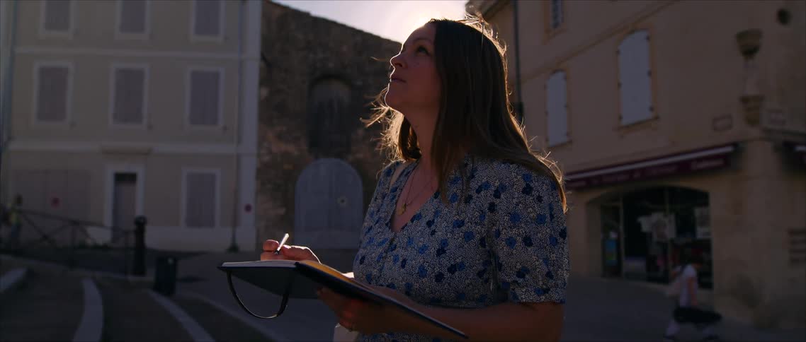 Woman in blue dress writes in notebook under bright sunlight in europeanstyle street