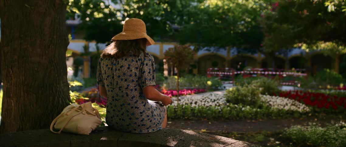 Woman sitting in a flower garden reading under the shade of trees