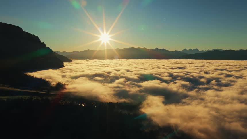 Sun glares from the sky onto the fog covered valley and the swiss mountains