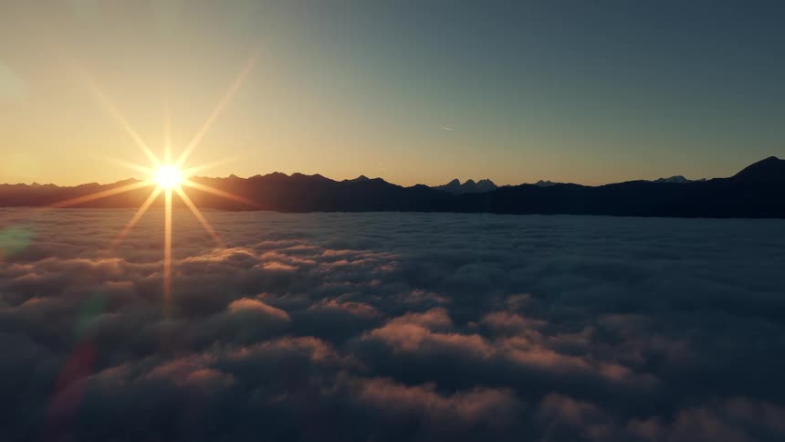 Sun sets behind mountains lighting clouds below with golden and deep blue tones