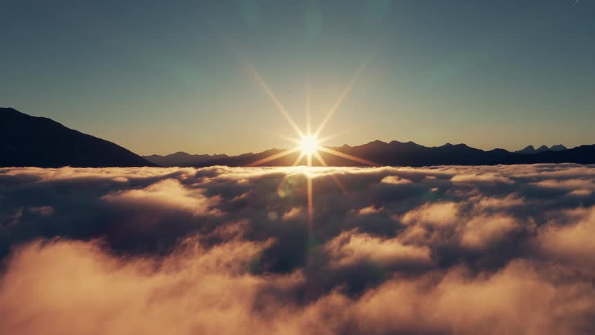 Aerial of bright sun rising on the horizon over the mountains