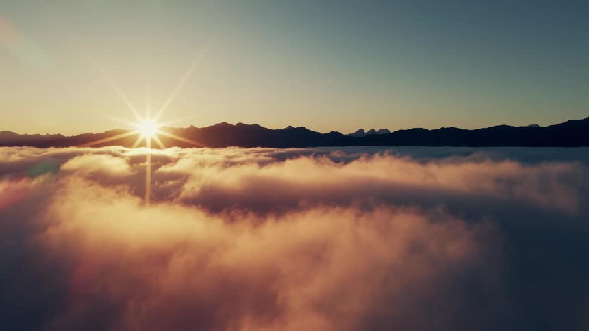 Aerial of bright shining sun rising on the horizon over the mountains