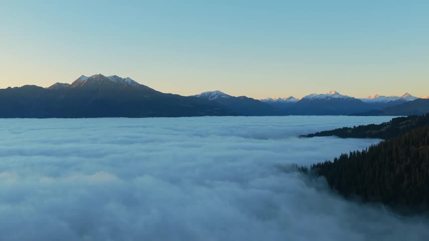 Snowy mountain range under clear sky rises above a fogcovered valley