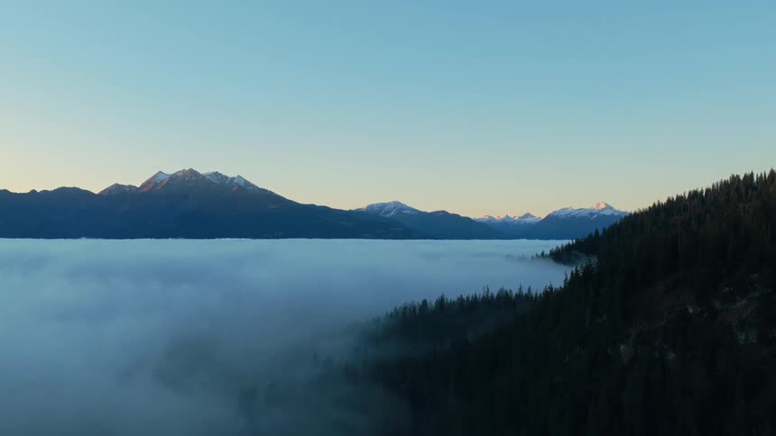 Snowcovered peaks glow above a fogfilled valley
