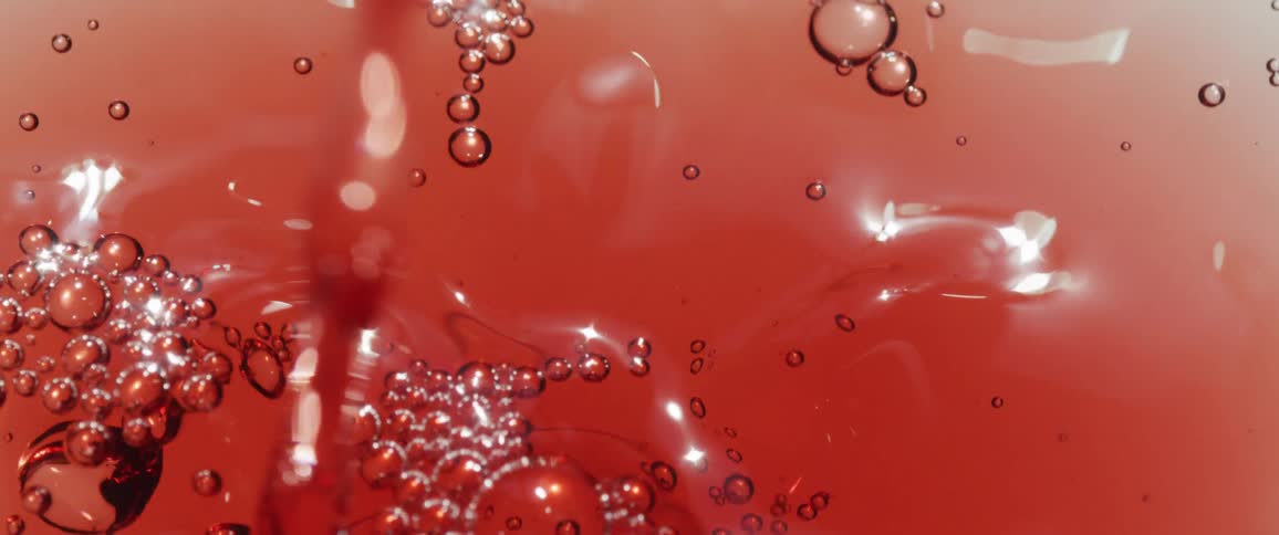 Foamy red liquid forms glistening bubbles as its poured
