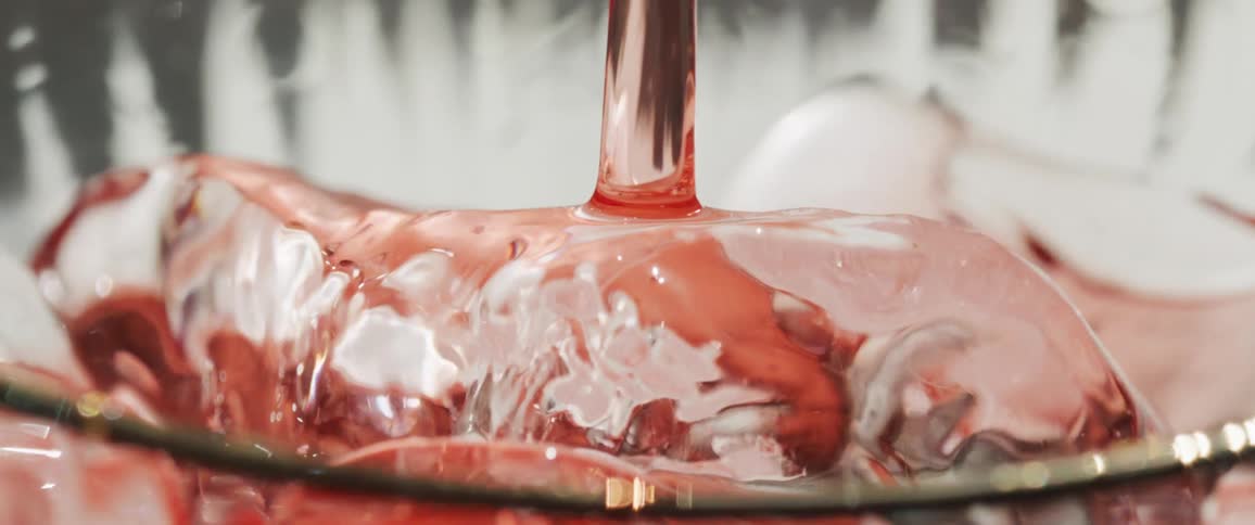 Red liquid is poured over ice in a cup