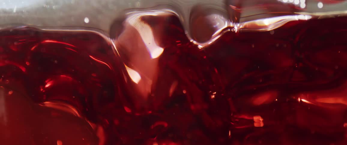 A closeup view shows a reddishbrown viscous liquid sloshing inside a clear container causing waves and reflections on the surface and against the container walls