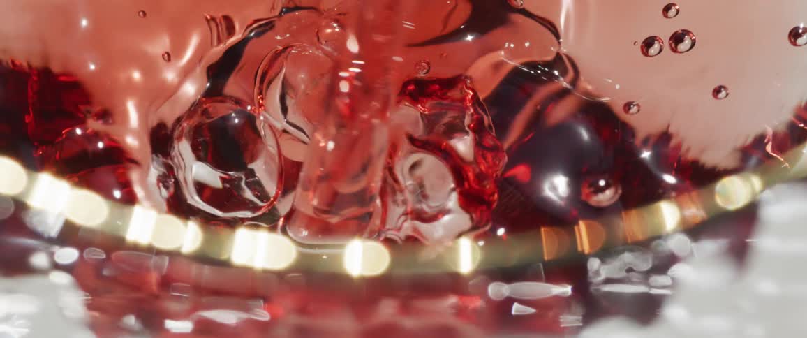 Red beverage flows into a clear glass