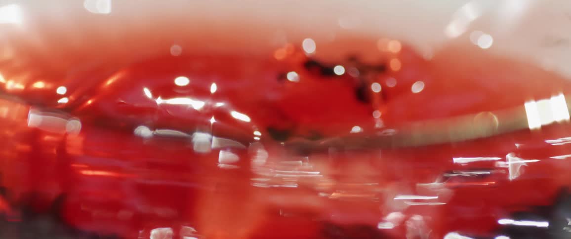 Close up of an ice cube dropping into red liquid beverage