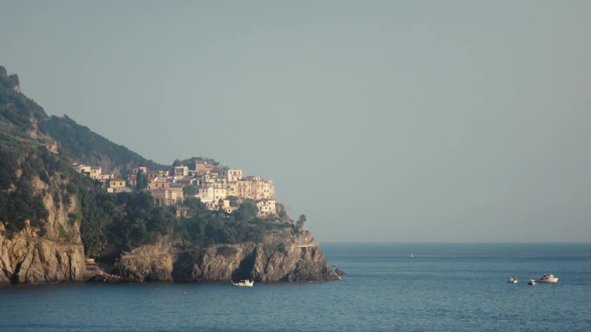 Lightcolored buildings cluster on a green cliff overlooking blue sea under clear sky