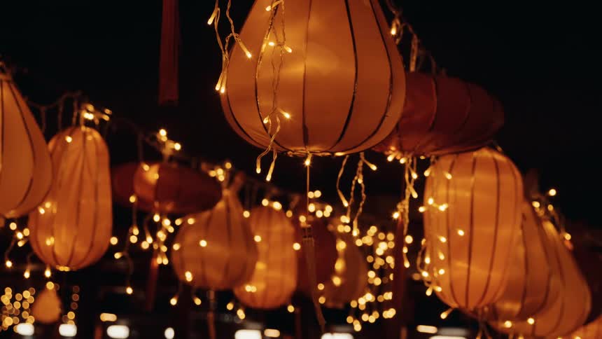 A street glows at night as carnival lamps line both sides casting colorful light across the pavement and creating a festive atmosphere under the dark sky