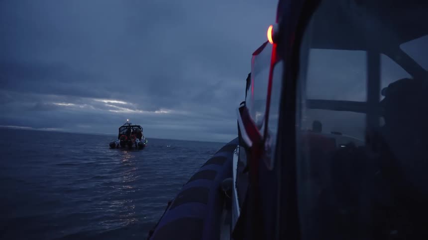 Two boats sit anchored together in the middle of the ocean on a cloudy evening their hulls gently rocking as overcast skies cast a moody reflection across the water