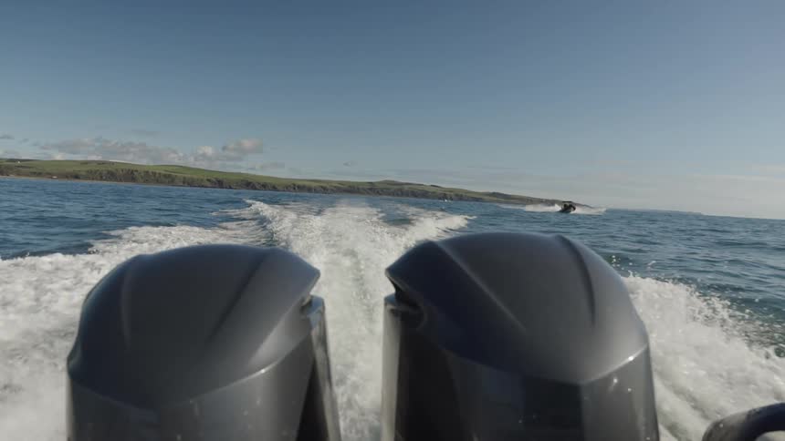 A twinengine boat speeds across the ocean at midday slicing through waves with power and precision as another boat trails behind closing in from the distance under the bright sun