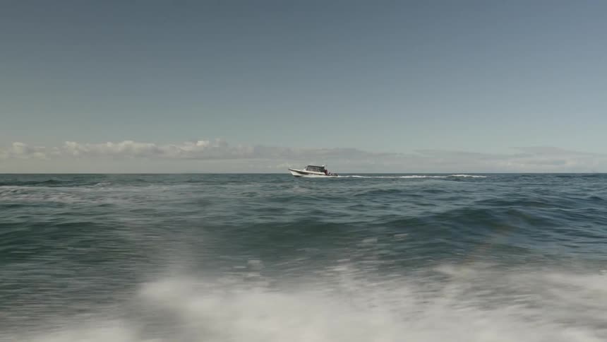 A speed boat races across the ocean at midday its hull slicing through the waves as sunlight glints off the water and a trail of white spray fans out behind it