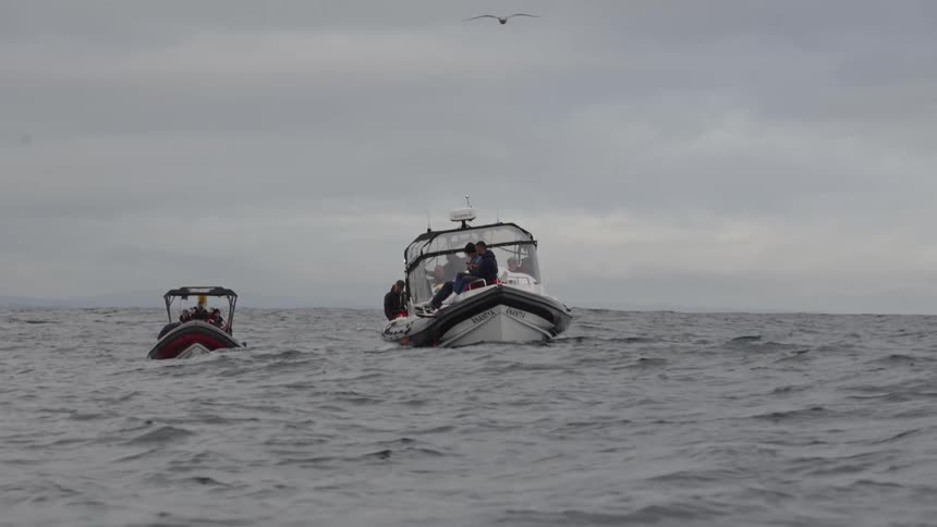 Two boats sail close together in open sea under a cloudy sky