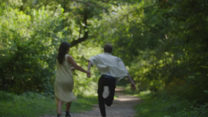 A young couple runs hand in hand down a forest path