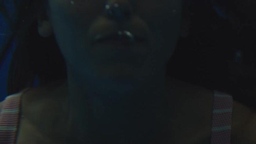 Woman floating underwater removes her goggles and swims towards the surface