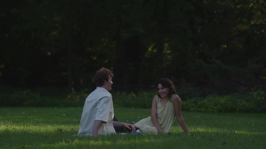 Man and woman sitting on the lawn near the woods smile and talk