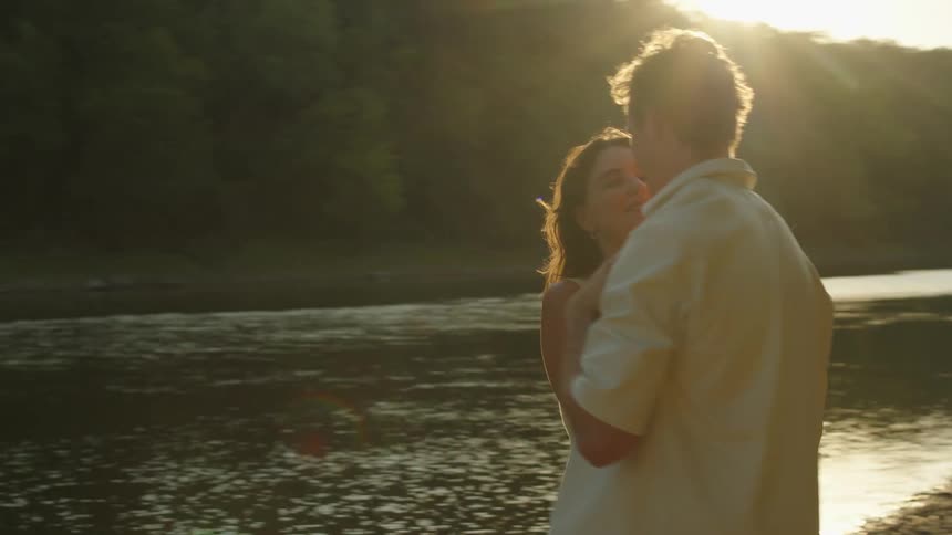 A couple dances romantically on a rocky shore at sunset