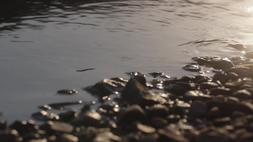 Extreme closeup of water lapping a rocky shore at golden hour