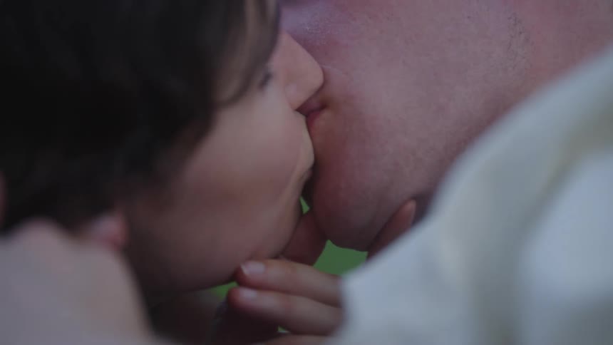 Woman pulls a man in by his chin to share a kiss on a summer day