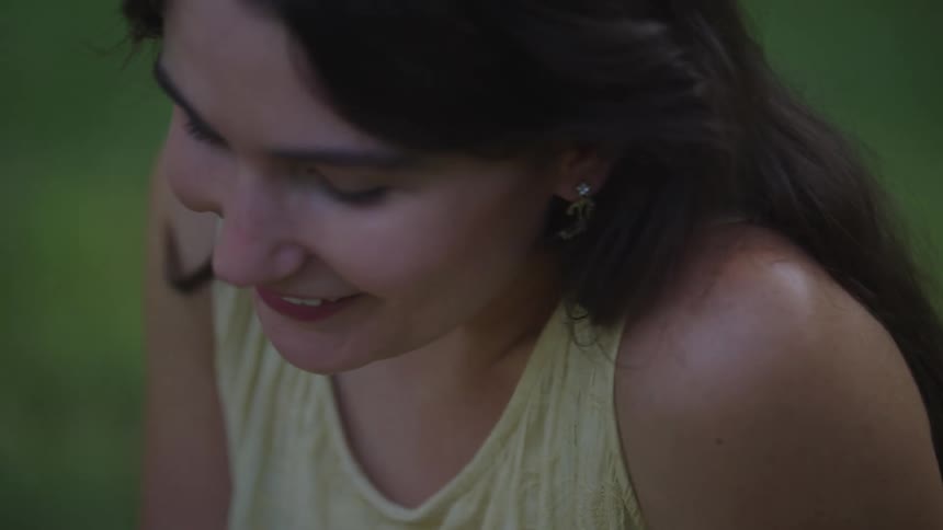 Woman smiles softly while looking down in a green field
