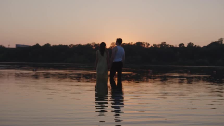 Couple watches the sunset while standing in shallow water