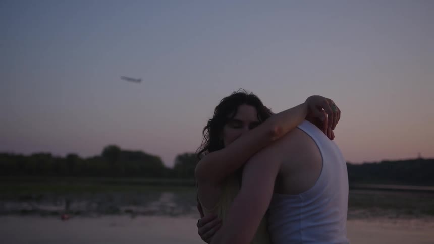 Couple slow dances on the riverbank after dusk