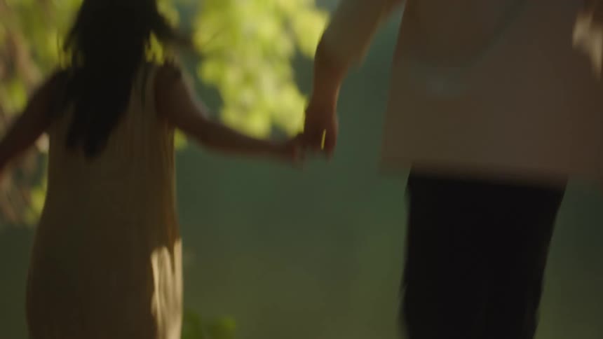 A couple runs on a rocky riverbank toward the water surrounded by green foliage
