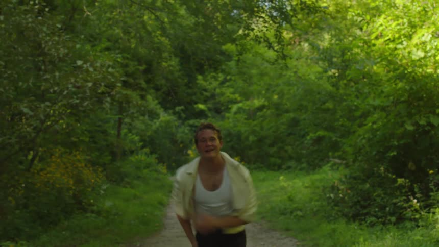 Couple stop hugging on a trail through the woods and start running playfully