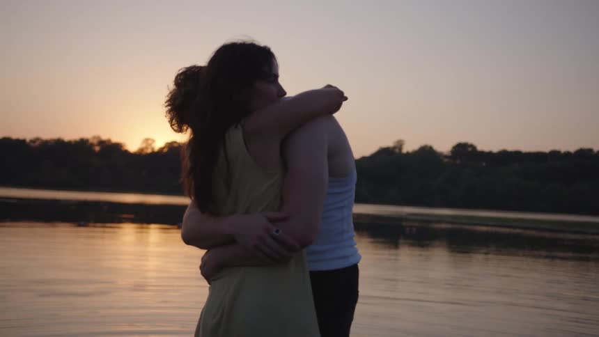 Romantic couple embracing at the riverside silhouetted against the horizon at sunset