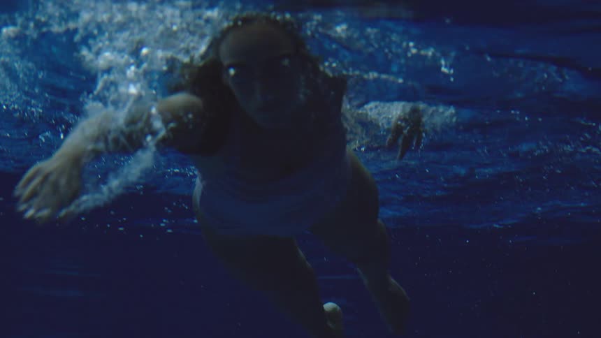 Woman swims underwater in a blue pool moving amid bubbles