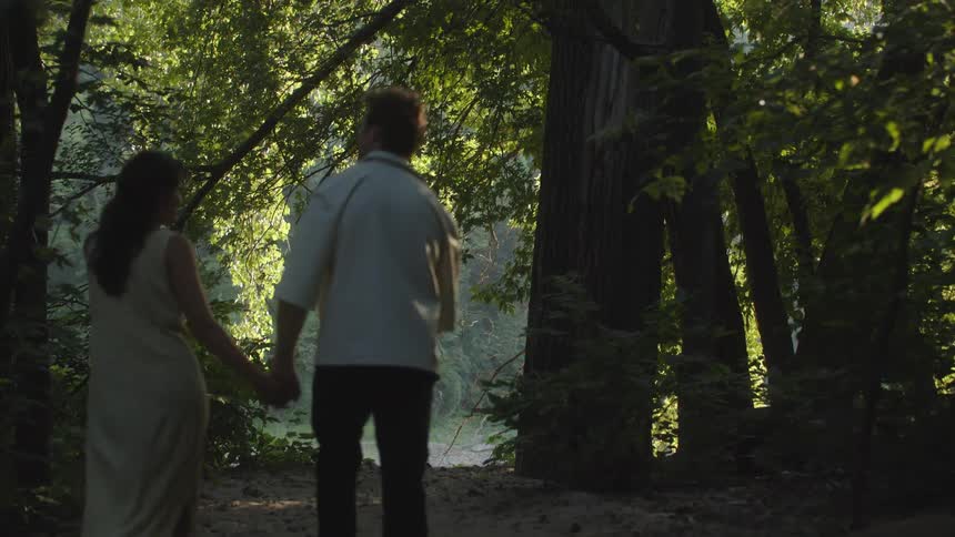 Couple walks arm in arm along a shaded path surrounded by trees