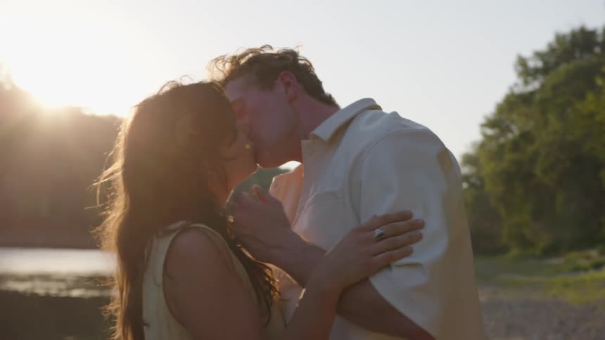 Couple standing on the riverbank near the woods kisses