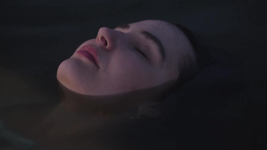 Woman floats with closed eyes in calm water at nightfall