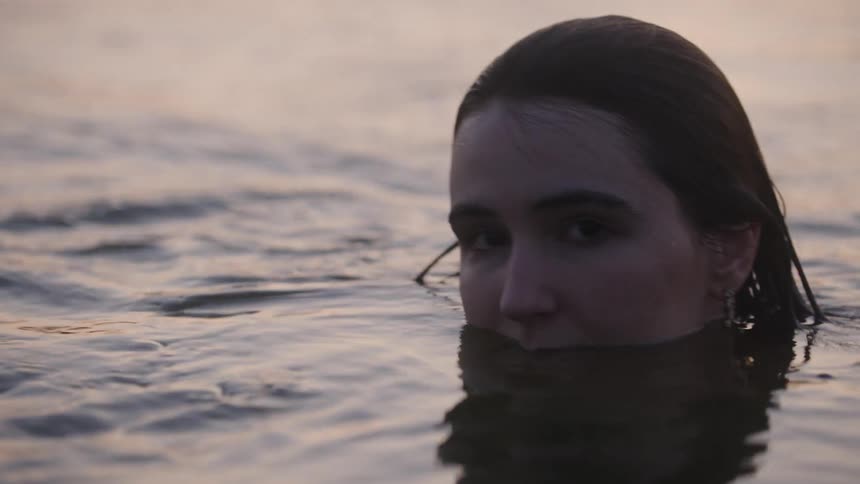 A young woman swims in the ocean at midday her body fully submerged with only her head visible above the water at sunset