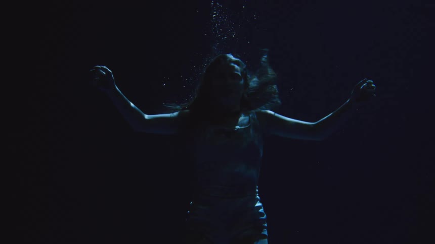 A young woman swims fully submerged beneath the ocean at night her silhouette gliding through the dark moonlit water as gentle currents ripple around her