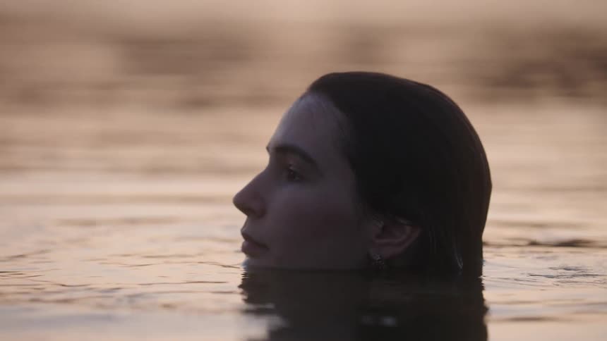 Woman floats in calm water under the soft light of dusk