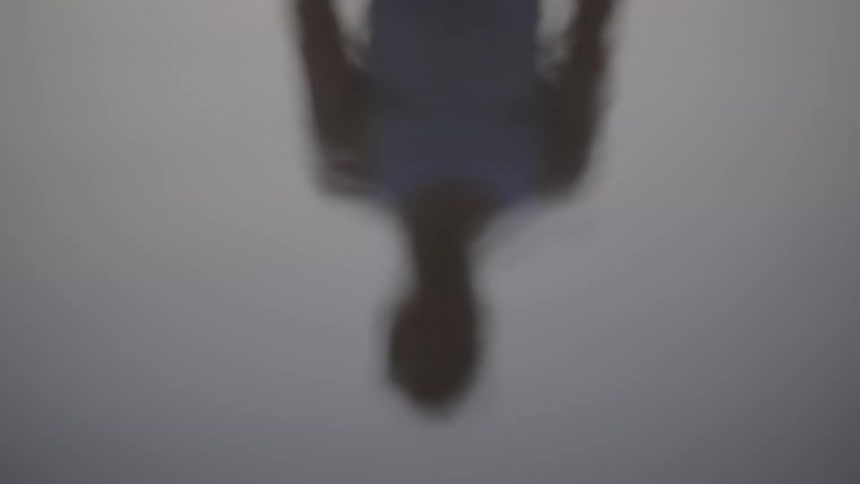 The dark blurry upside down silhouette of a person is suspended over still water creating a perfectly mirrored image in a pale gray and abstract scene