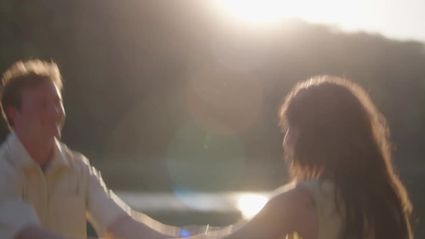 Young happy couple dancing by the river at sunset