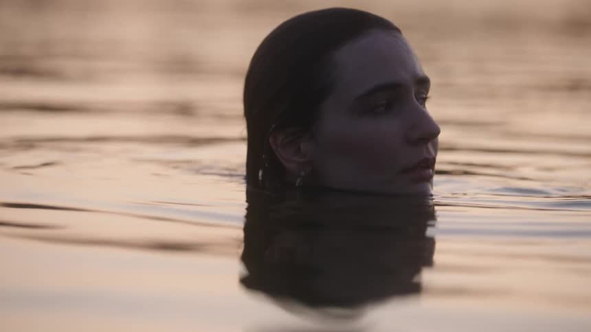 Woman treads water tinted red by sunlight creating ripples