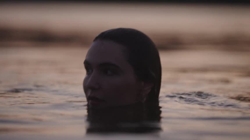 Woman swims calmly with her face partially submerged in water gilded by the evening light