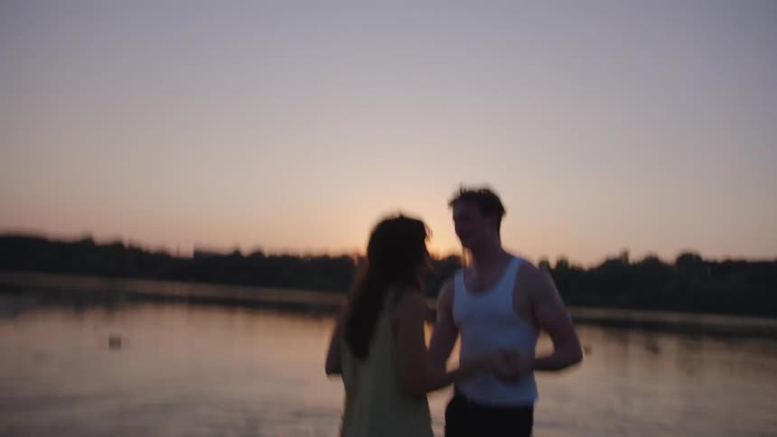 Couple holding hands in shallow water faces sunset with vegetation in the background