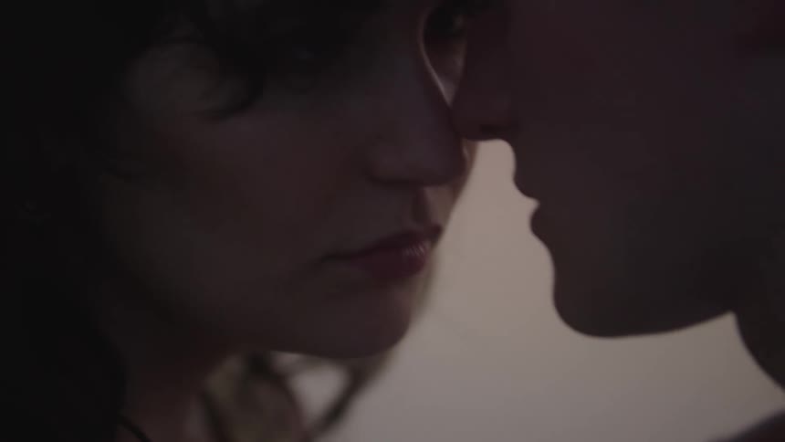 A young couple stands outdoors at sunset gently touching their faces together in a romantic moment as warm light bathes the scene in golden hues